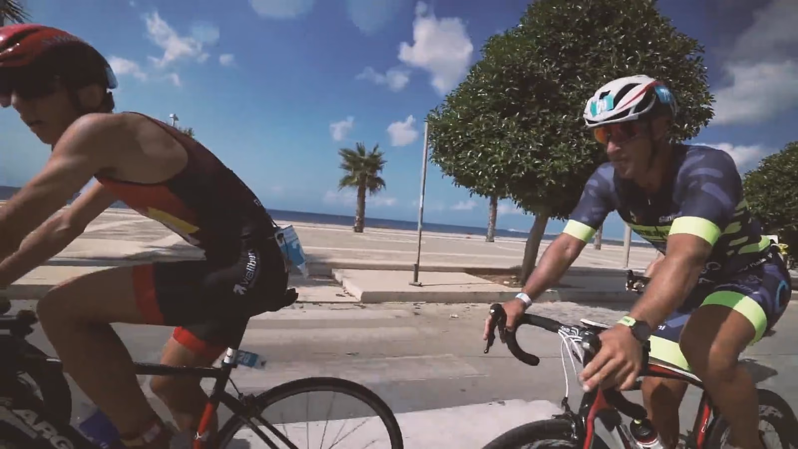 Un atleta in bici sul lungomare, con il mare e le palme alle spalle